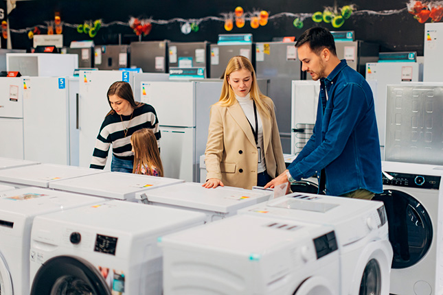 drie mensen staan in de winkel om wasmachines met elkaar te vergelijken
